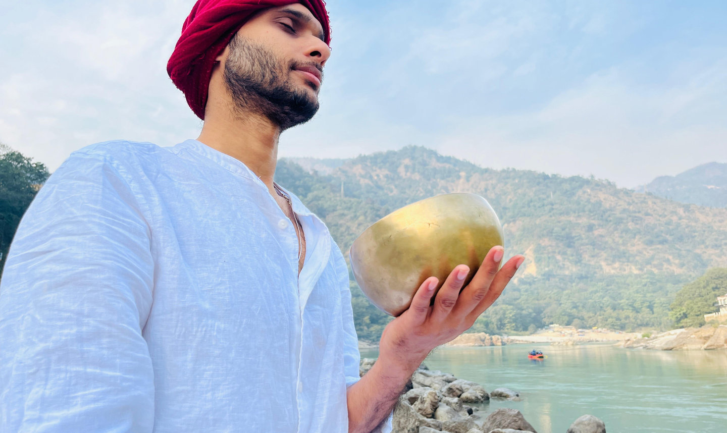 Tomojit holding a Himalayan singing bowl by the Ganga in Rishikesh